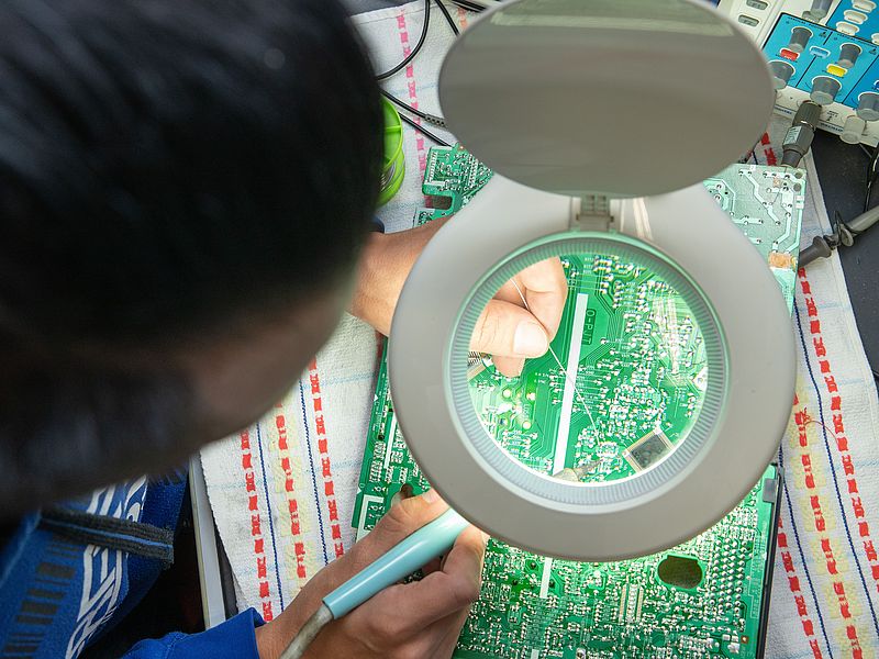 One person solders a circuit board.