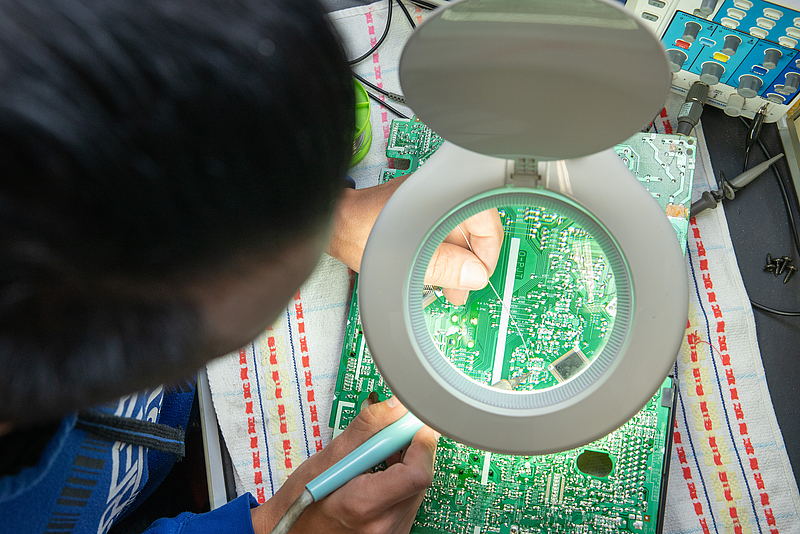 One person solders a circuit board.