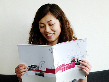 Junge Frau liest lächelnd in einer Publikation.