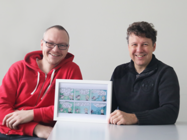 Zwei Männer halten ein Bild und  lachen in die Kamera