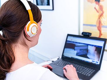 Eine Person mit Kopfhörern bei der Arbeit am Laptop.