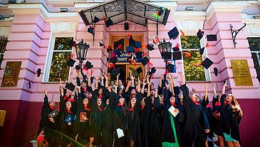 Studenten in einem Talar die ihre Doktorhüte in die Luft werfen