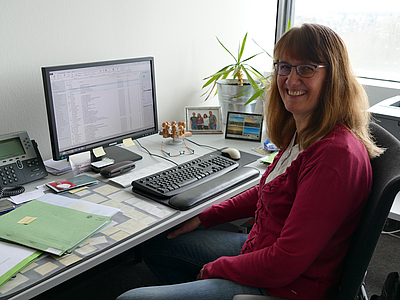 Foto von Silke Völkers, welche an ihrem Schreibtisch sitzt, mit Blick in die Kamera.