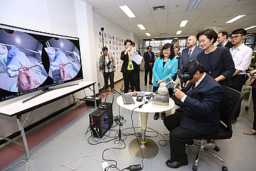 Man sitting in a chair testing virtual reality glasses. Spectators are standing around.