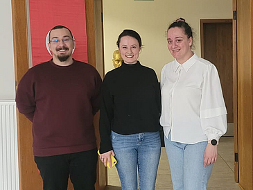 Seda Saban Dülger steht mit ihren Kolleg:innen Assistenzprofessorin Dr. Şadiye Back und Adnan GÜLAÇTI vor einer offenen Tür in den Räumlichkeiten der Universität Gazi in der Türkei.