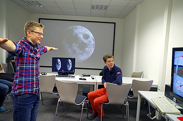 Junge steht vor dem Bildschirm. Ein weiterer schaut ihm zu