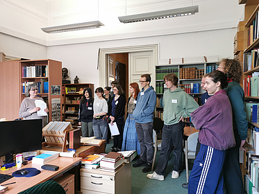 Studierende stehen in der Arbeitsstelle des Althochdeutschen Wörterbuchs und hören einer Mitarbeiterin zu.