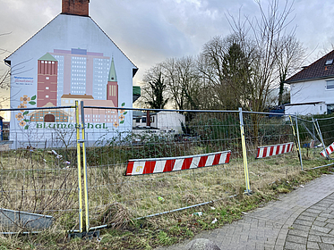 Das Foto zeigt eine Hausfassade in Bremen-Blumenthal mit einer Brache und einem Bauzaun davor.