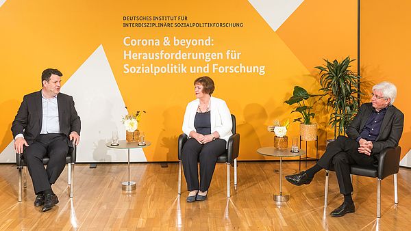 Zwei Männer und eine Frau sitzen vor einer Wand in einem Studio für eine Online-Eröffnung