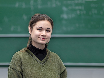Adela Talipov in front of a blackboard in a lecture hall.