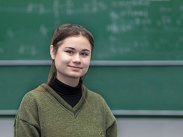 Adela Talipov in front of a blackboard in a lecture hall.
