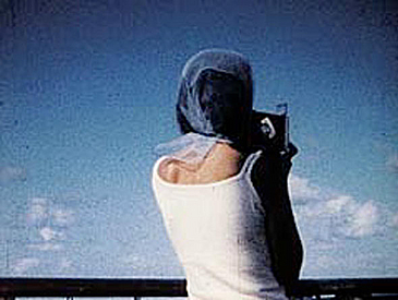 filmstill Frau mit Kopftuch von hinten gegen blauen Himmel