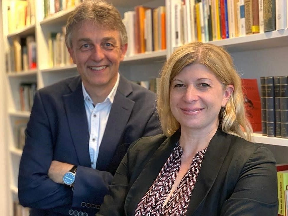 Zwei Menschen stehen vor einem Regal und blicken in die Kamera