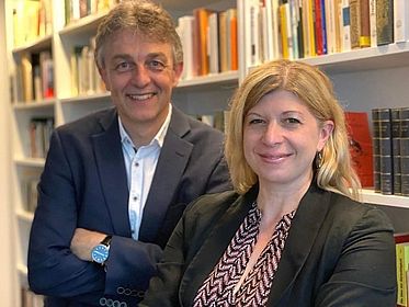 Zwei Menschen stehen vor einem Regal und blicken in die Kamera