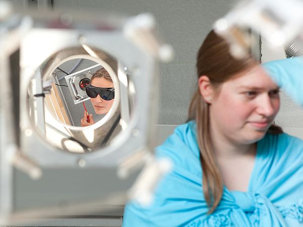 The face of a person wearing dark goggles viewed through a mirror.