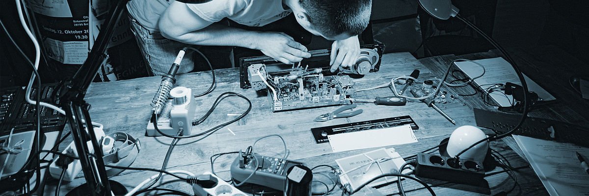 Abbildung eines Tisches mit technischen Geräten und Werkzeugen, Darstellung des Reparaturvorgangs technischer Geräte