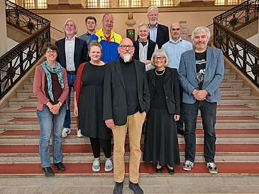 Elf Personen stehen auf einer breiten Treppe