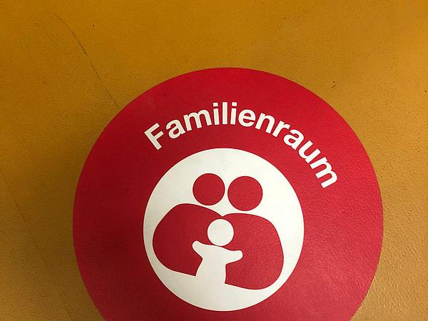 Auf dem Boden klebt ein Kreis mit einem Piktogramm einer Familie. Darüber steht "Familienraum".