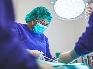 Photo from an operating theater shows woman with hood and mask