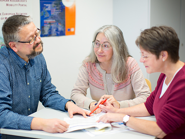 Drei Personen im Gespräch an einem Tisch.