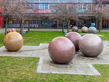 Große Granitsteinkugeln stehen verteilt auf einer Grünfläche vor einem Gebäude