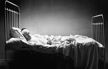 s/w filmstill Mann mit Kopfverband liegt formatfüllend in einem Gitterbett