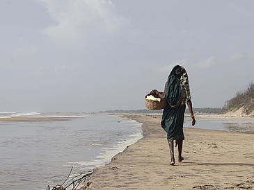Eine Person trägt einen Weidenkorb an einem Strand entlang