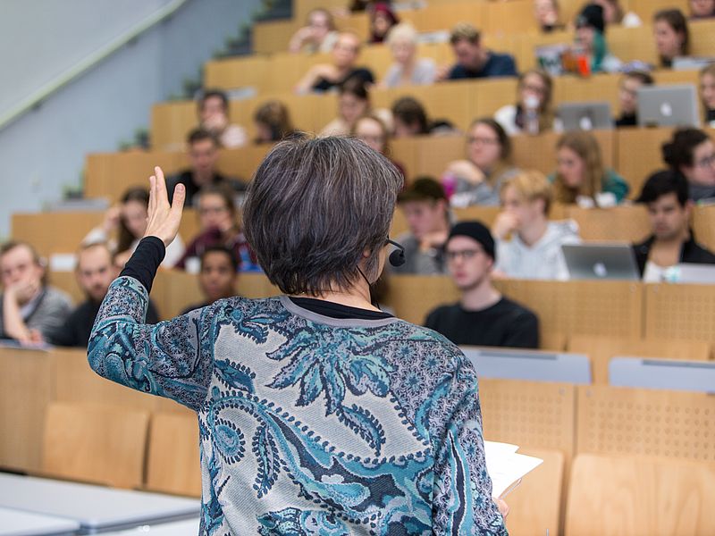 A lecturer speaks to an audience in a packed lecture hall.