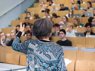 Eine Lehrende spricht vor Zuhörern im vollen Hörsaal.