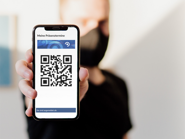 Junger Mann mit Alltagsmaske zeigt Handy mit QR-Code