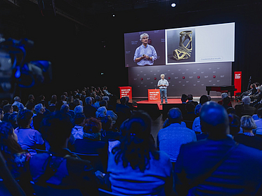 Bild vom Falling Walls Science Summit: Person auf der Bühne mit großen Bildschirmen, davor Publikum