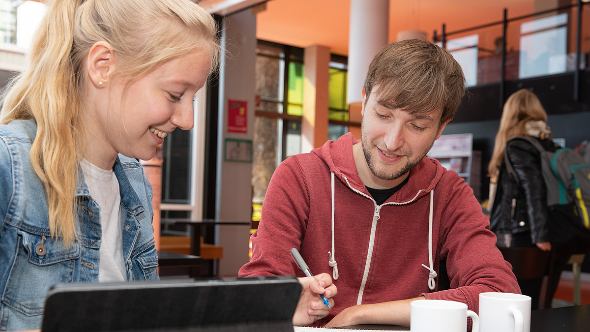 Zwei Studierende sitzen in der GW2-Cafeteria und lernen
