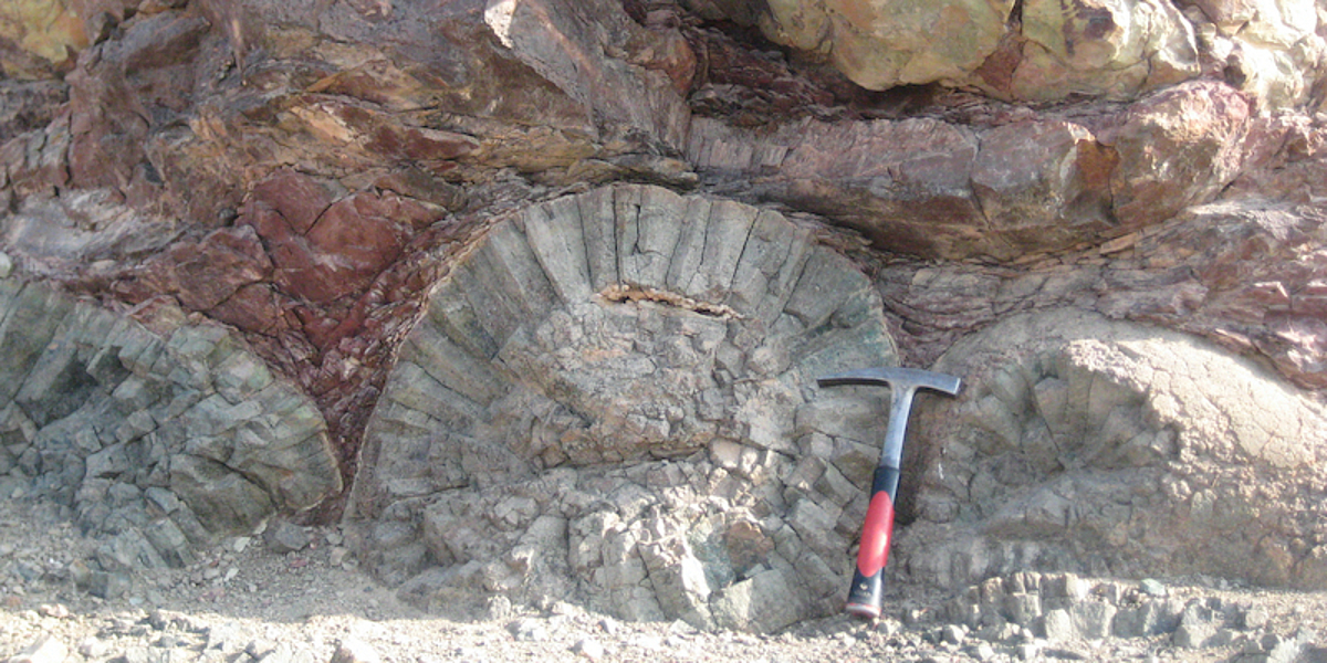 Bild einer Gesteinsformation im Oman, zum Größenvergleich ist neben der Gesteine ein Geologenhammer zu sehen.