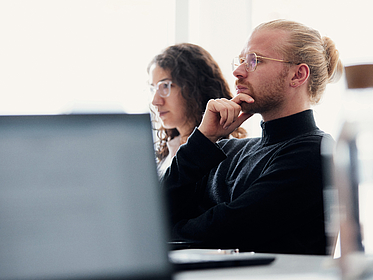 Zwei Personen schauen nachdenklich nach vorne und folgen einem Vortrag