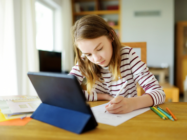 Mädchen sitzt vor einem Tablet zu Hause und lernt