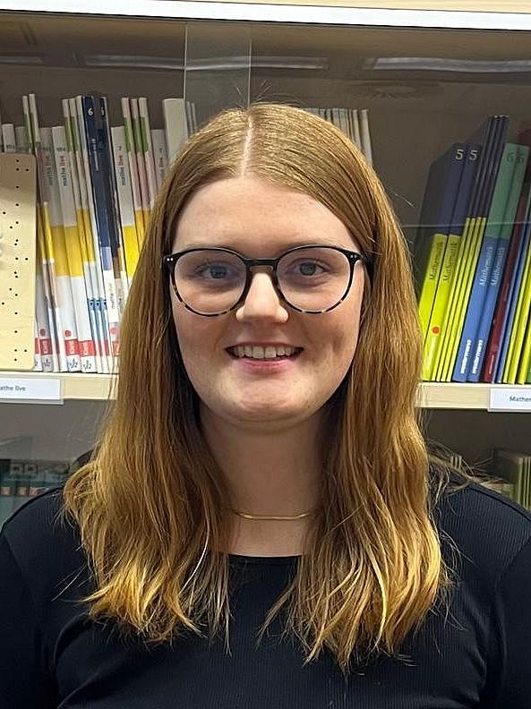 Eine Person steht lächelnd vor einer Vitrine mit Schulbüchern