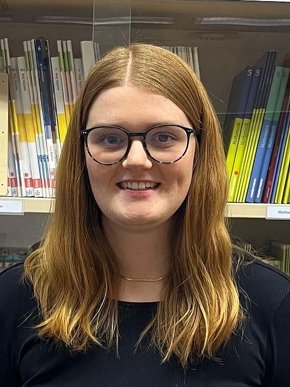 Eine Person steht lächelnd vor einer Vitrine mit Schulbüchern