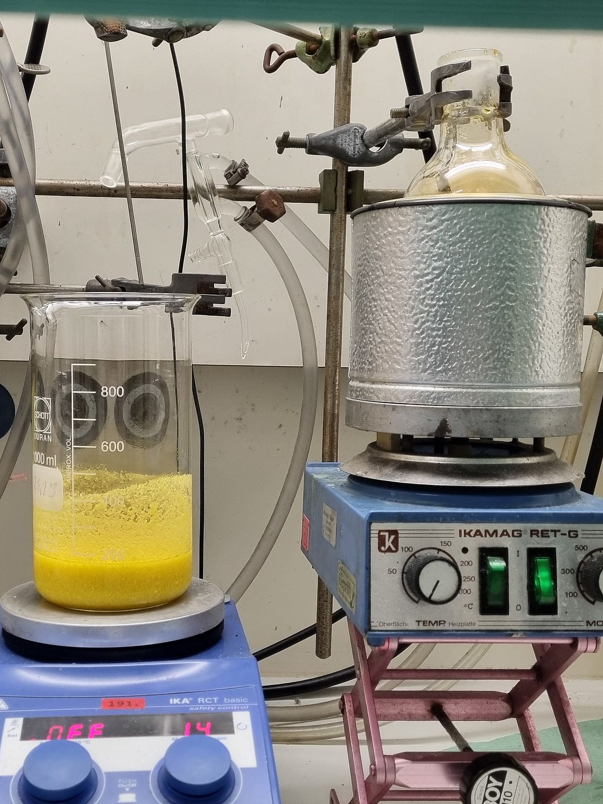 The picture shows various pieces of equipment in a fume hood in the lab. There are three hot plates, along with a flask, a beaker, and a Dewar flask containing a flask.
