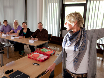 Eine Lehrende vor einer Gruppe Zuhörer in einem Seminarraum.