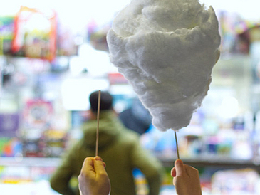 One person holds a candy floss stick without candy floss in one hand and a white candy floss on a stick in the other.