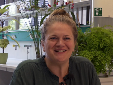 Anna Beniermann wird in einem Labor gefilmt. Im Hintergrund sind Pflanzen und Labormaterial zu sehen.