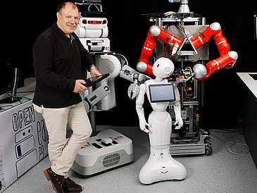 Mann steht neben drei Robotern.