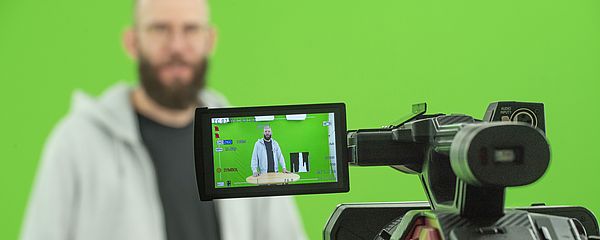 A man in front of a green screen is looking into the camera.