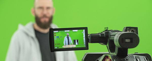 A man in front of a green screen is looking into the camera.