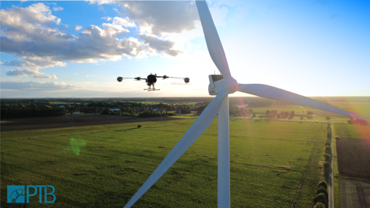 Drohne neben einer Windkraftanlage über einem grünen Feld
