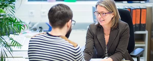Zwei Personen im Gespräch an einem Bürotisch.