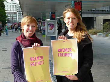 Zwei Frauen zeigen auf dem Uni-Boulevard Plakate