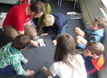 Ein Erwachsener und einige Kinder führen auf dem Boden sitzend Experimente durch.