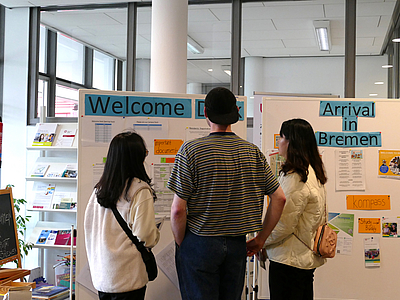 Drei Personen stehen vor der Info-Tafel des Welcome Desk