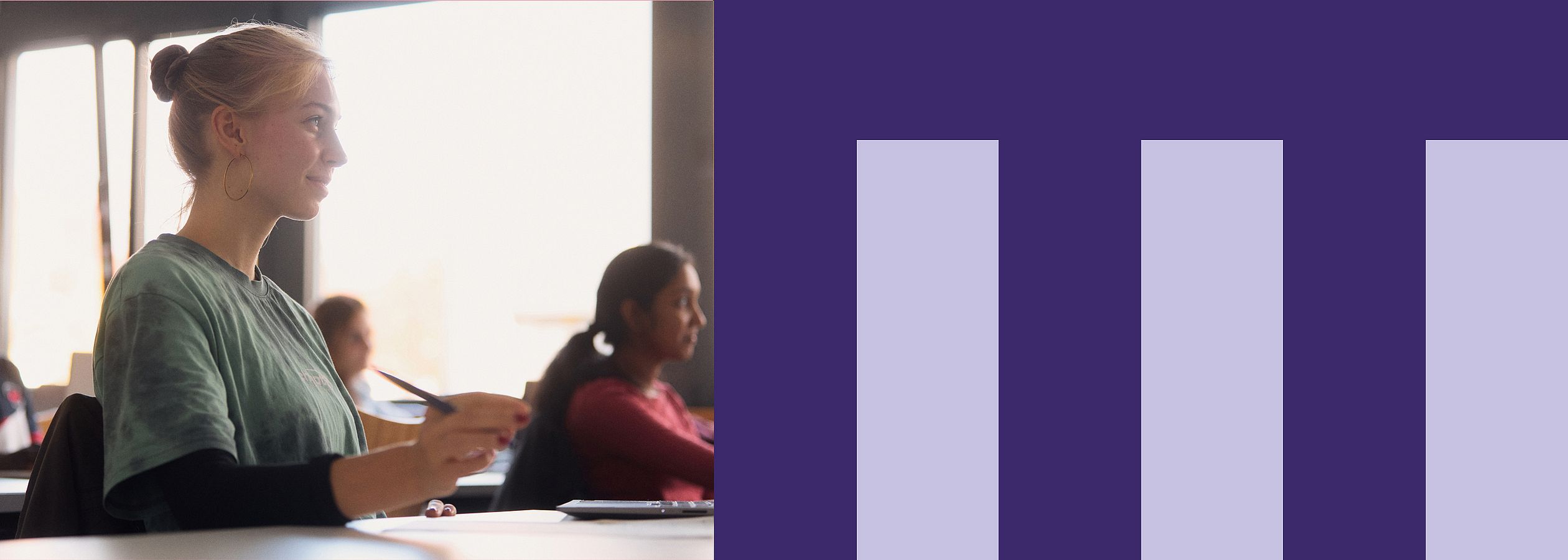 Eine junge Frau sitzt in einem Seminarraum mit anderen Menschen und schaut interessiert nach vorne.